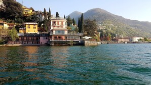 A waterfront property with a balcony overlooking a lake, surrounded by buildings and a mountain in the background. - Meridiana Boutique Hotel (Bellano)