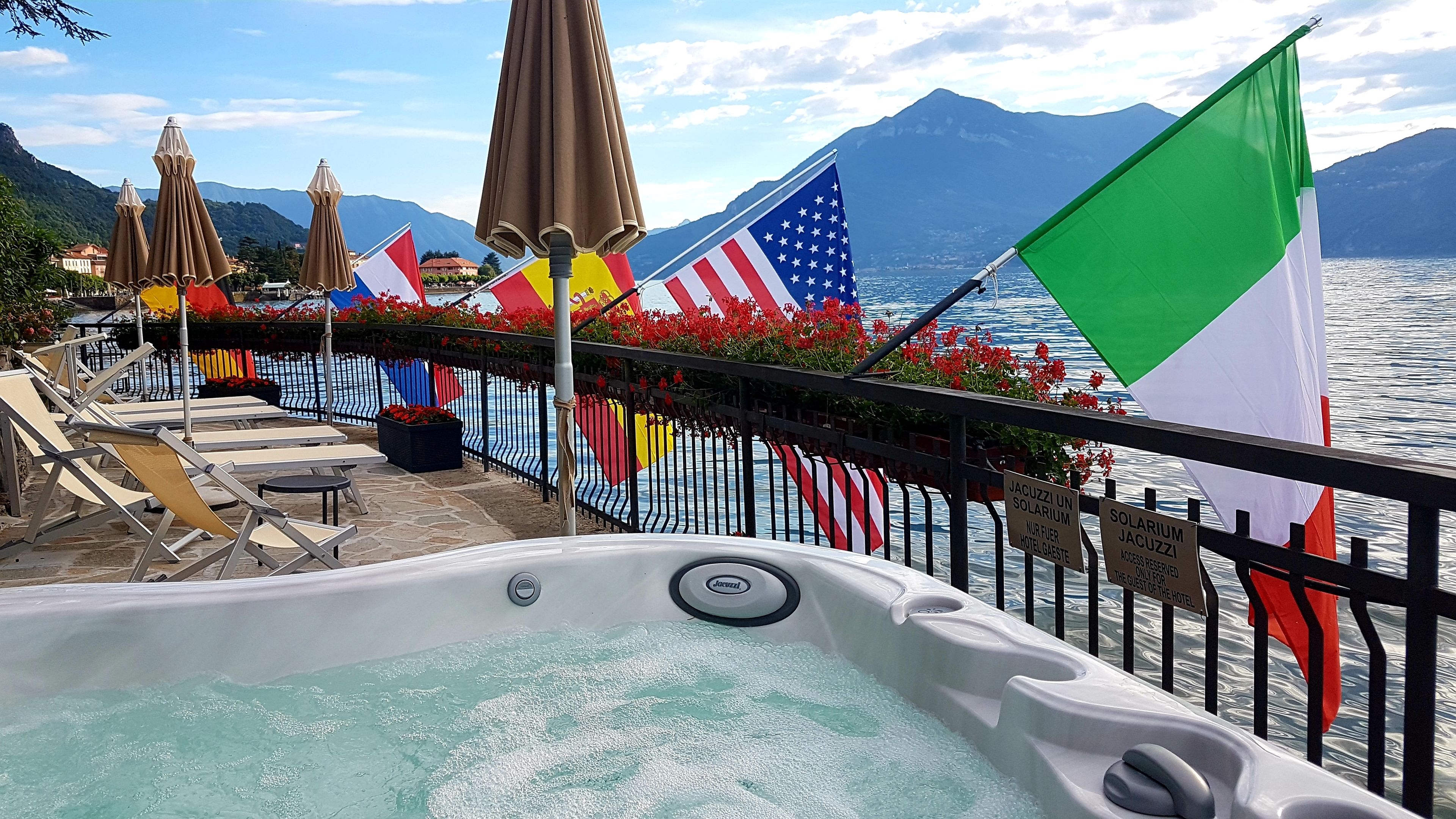 Een hottub met uitzicht op een meer en bergen, omringd door vlaggen en ligstoelen.