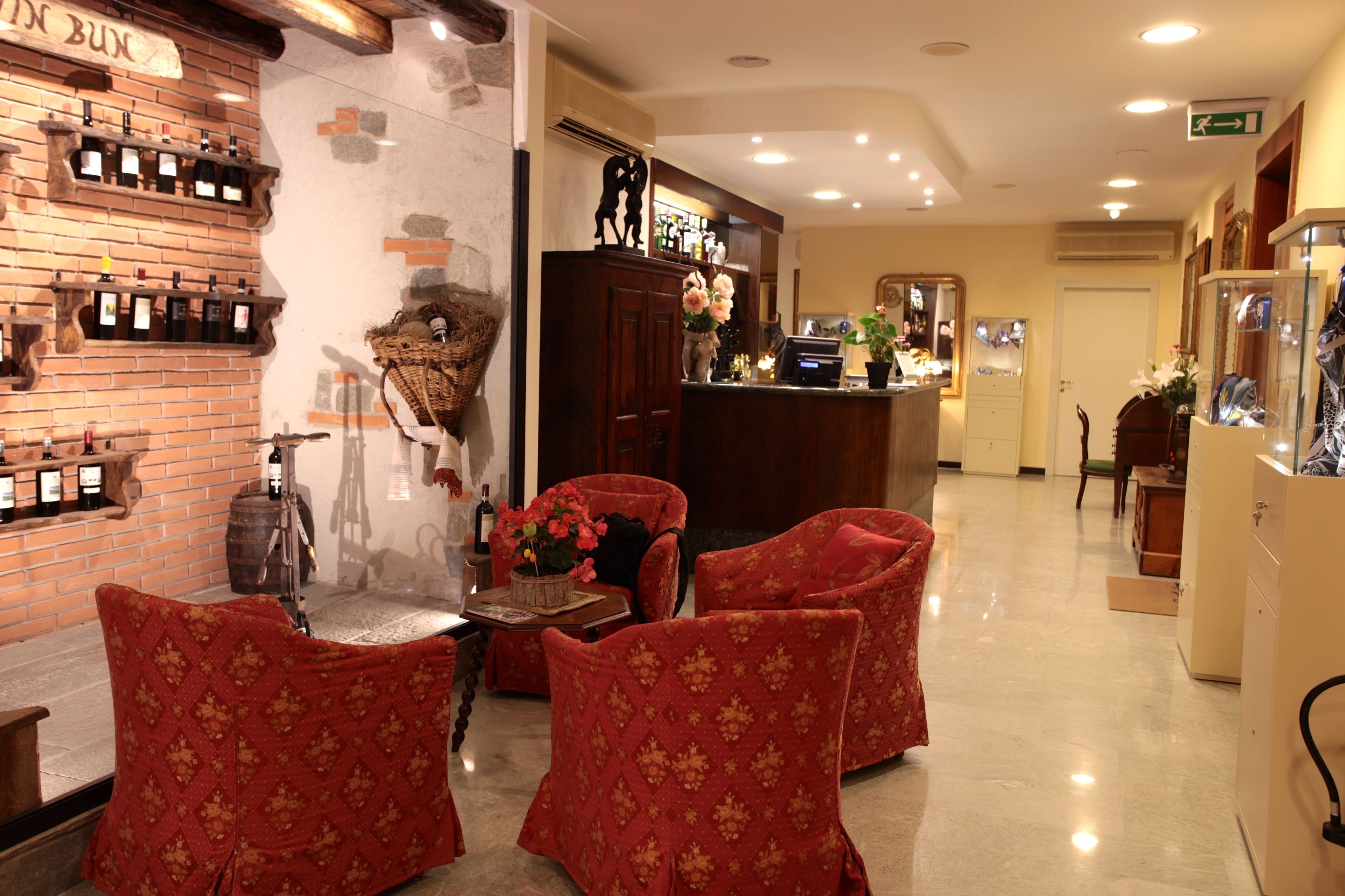 Un hall d’hôtel avec un mur en briques, un comptoir d’accueil et des fauteuils rouges recouverts de tissu.