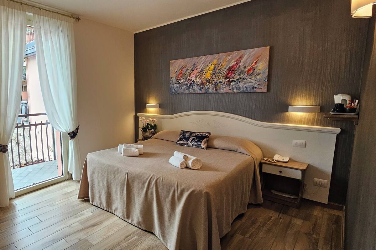 A hotel room with a bed, bedside lamps, a painting on the wall, and a view of the outside balcony.