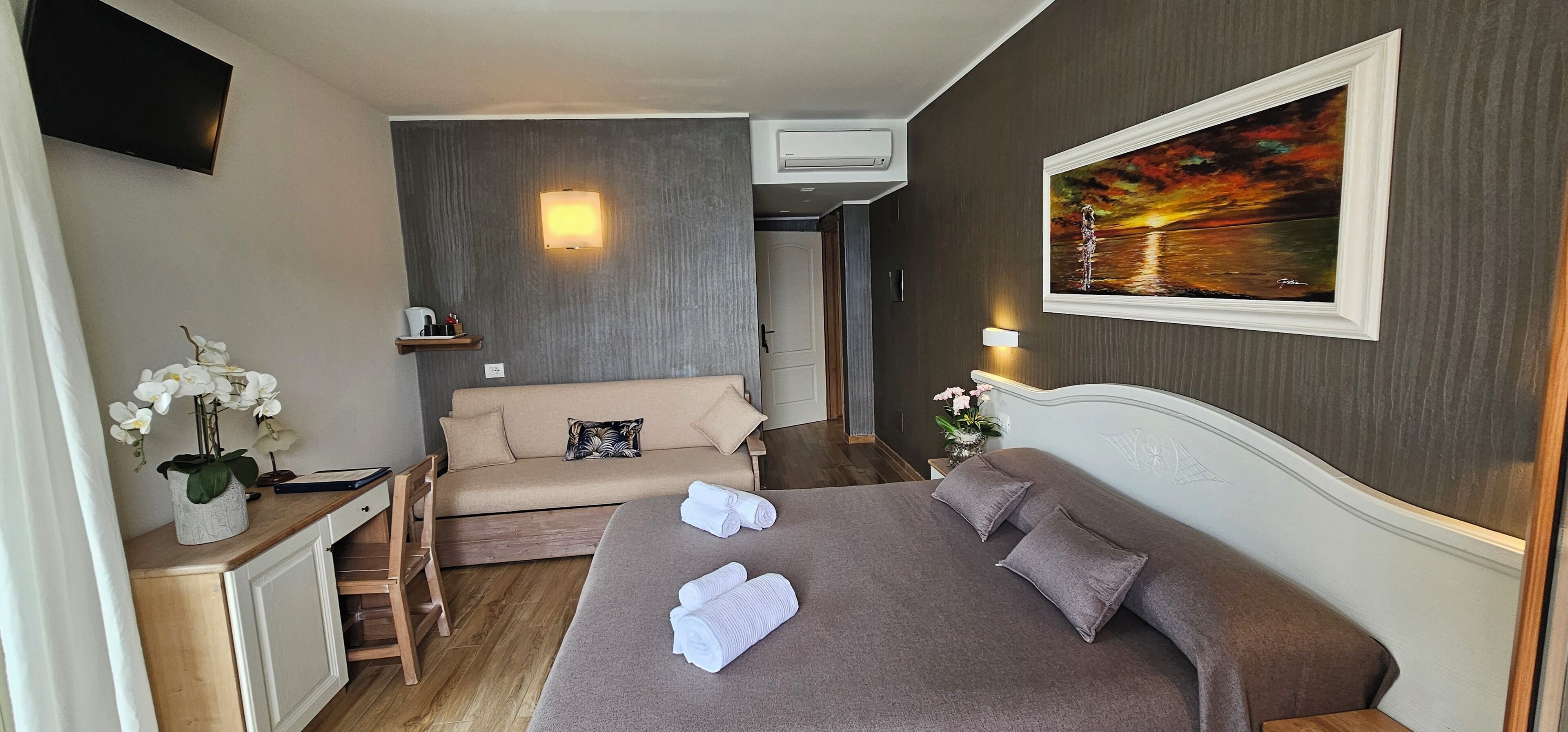 Hotelkamer met een bed, een bank, een bureau, een televisie en een schilderij aan de muur.