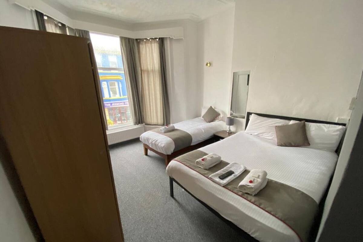 A hotel room with two beds, a wardrobe, a window with curtains, and a TV.