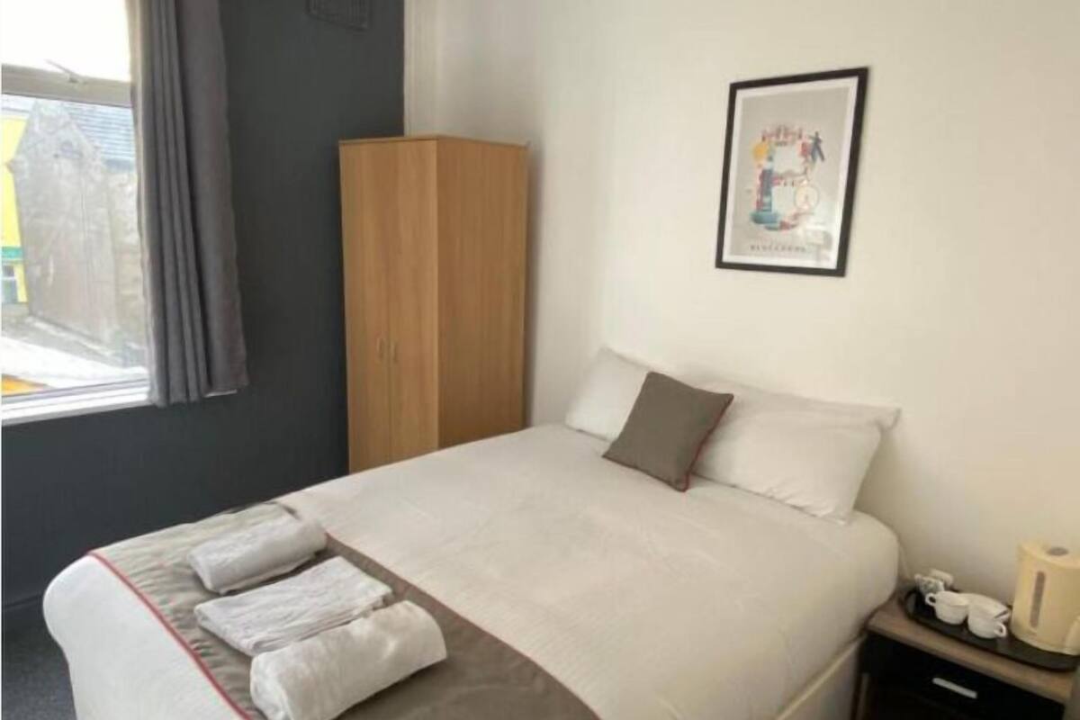 A hotel room with a large bed, a wardrobe, a framed picture on the wall, and a window with curtains.