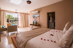 A hotel room with a large bed, a view of the pool, and a desk with chairs. - Villa Boudha (Sidi Abdallah Ghiat)