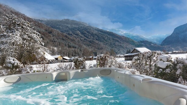Ein Whirlpool mit Blick auf die Berge, umgeben von schneebedeckten Bäumen und Häusern.