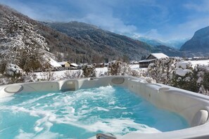 Un bain à remous avec vue sur les montagnes, entouré d’arbres et de maisons couverts de neige.