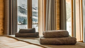 Ein Zimmer mit einem großen Fenster, Holzwänden, einem Bett mit Decke und zwei auf einer Matte gerollten Handtüchern.