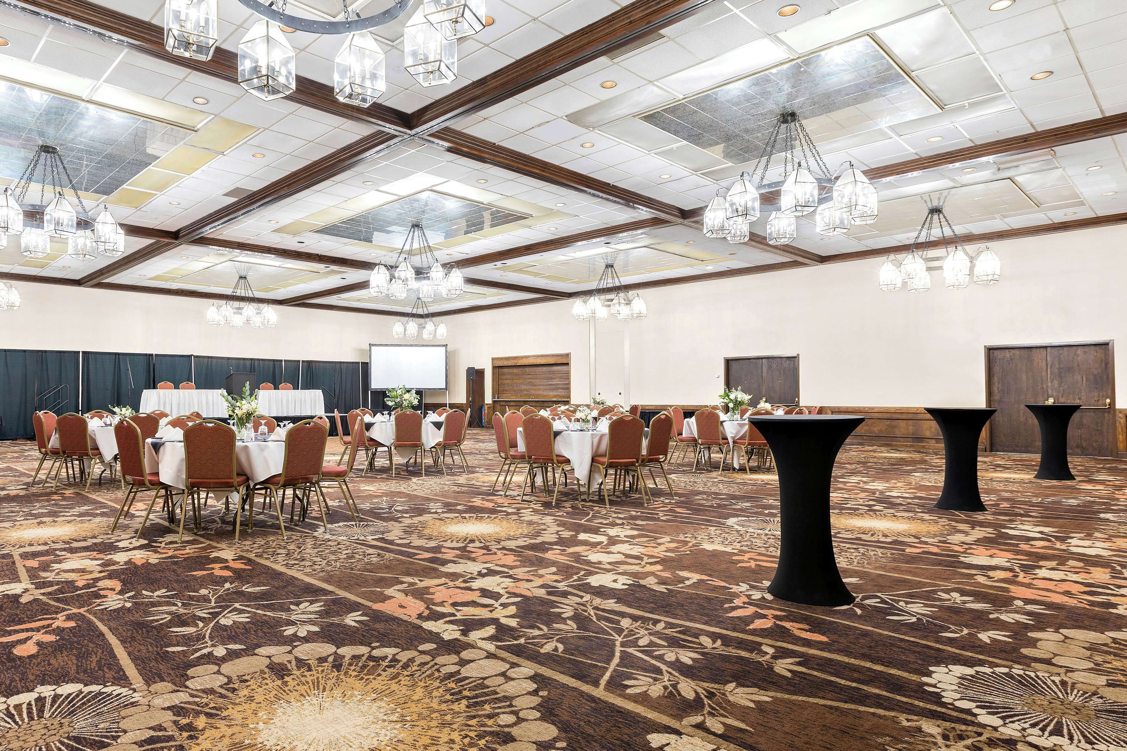 A large conference room with round tables, chairs, and a carpeted floor.