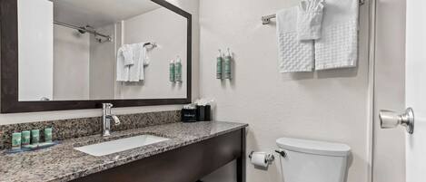 A bathroom with a granite countertop sink, a large mirror, a white toilet, and two towels hanging on hooks.