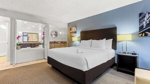 A hotel room with a large bed, a nightstand with a lamp, a wall-mounted mirror, and a view of the bathroom. - Best Western Downtown Casper Hotel (Casper)