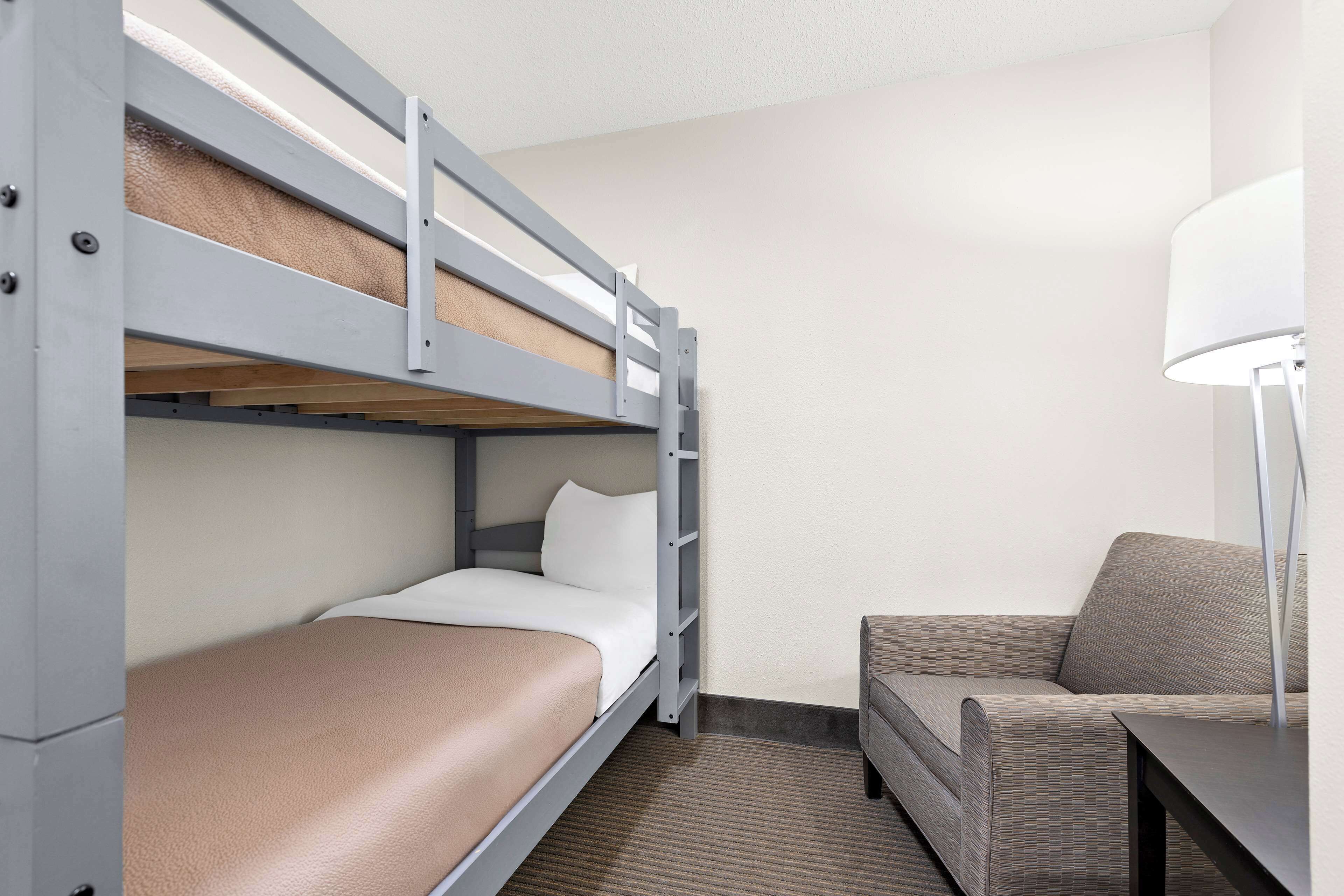 A hotel room with a bunk bed, a sofa, and a desk with a lamp.