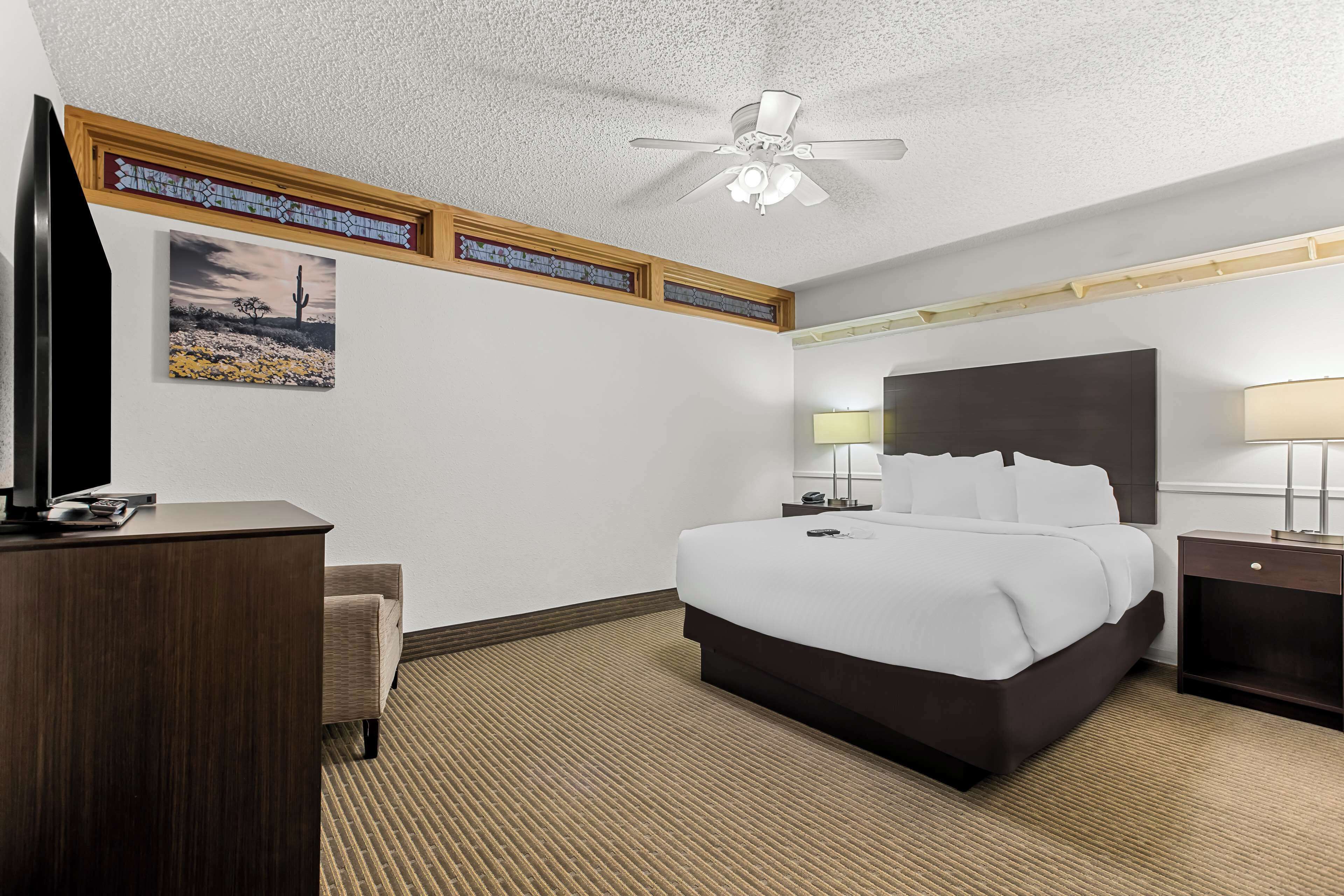 Habitación de hotel con una cama grande, un escritorio, una silla, un ventilador de techo y un televisor instalado en la pared.