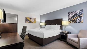 Habitación de hotel con cama, escritorio, silla, mesita de noche y dos lámparas fijadas a la pared.