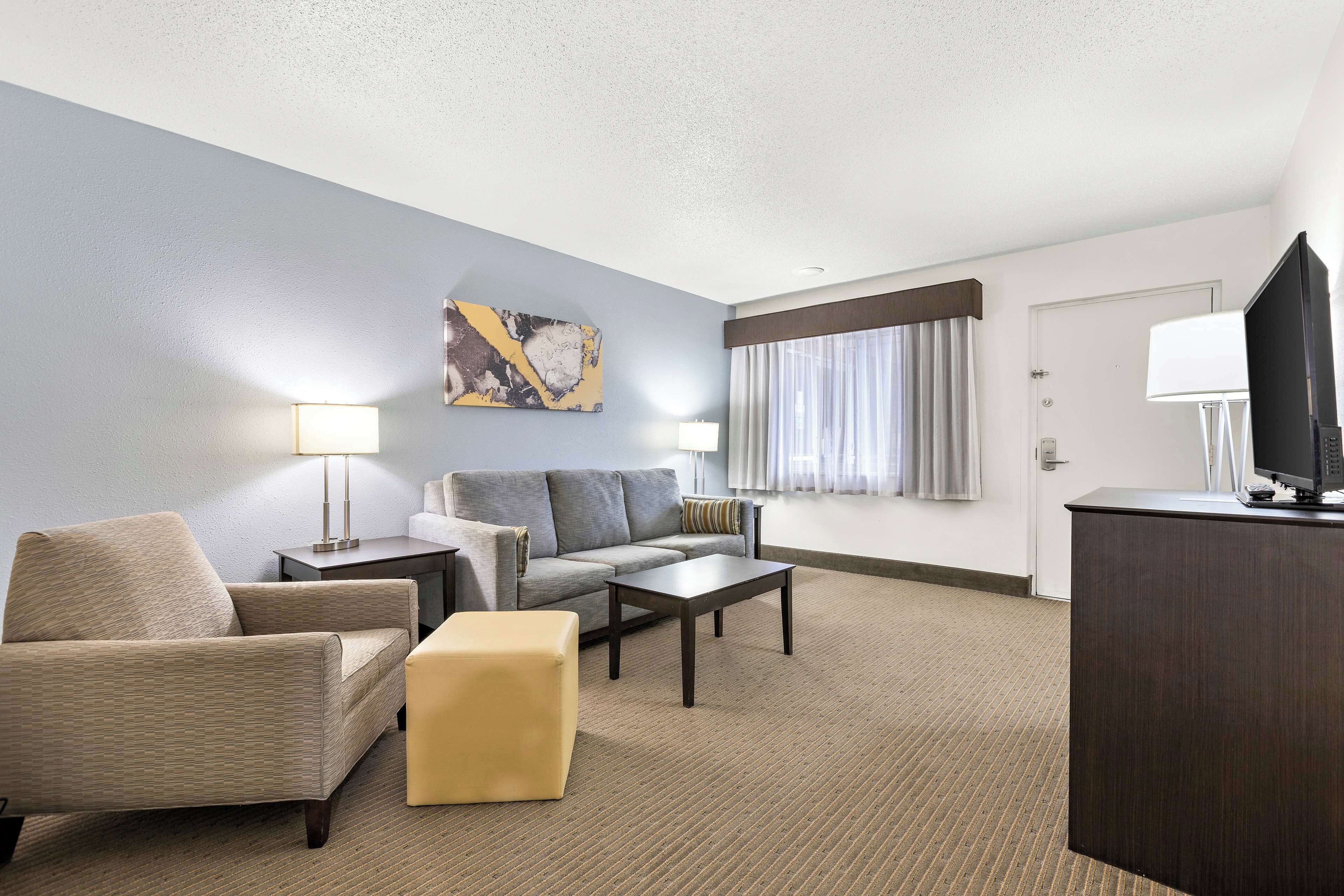 A hotel room with a sofa, armchair, ottoman, coffee table, TV, and artwork on the wall.