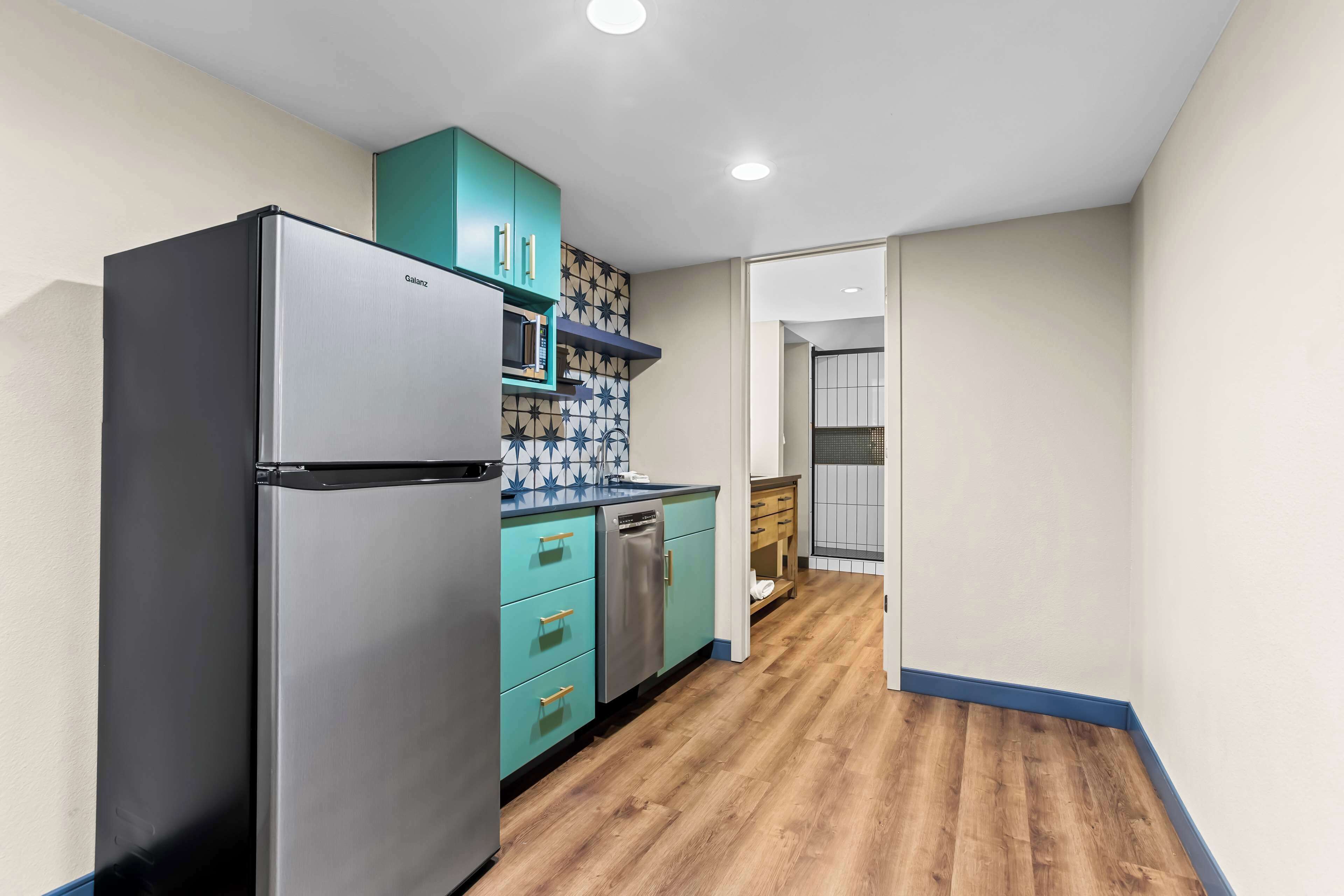 A compact kitchen with a refrigerator, microwave, and teal cabinets.