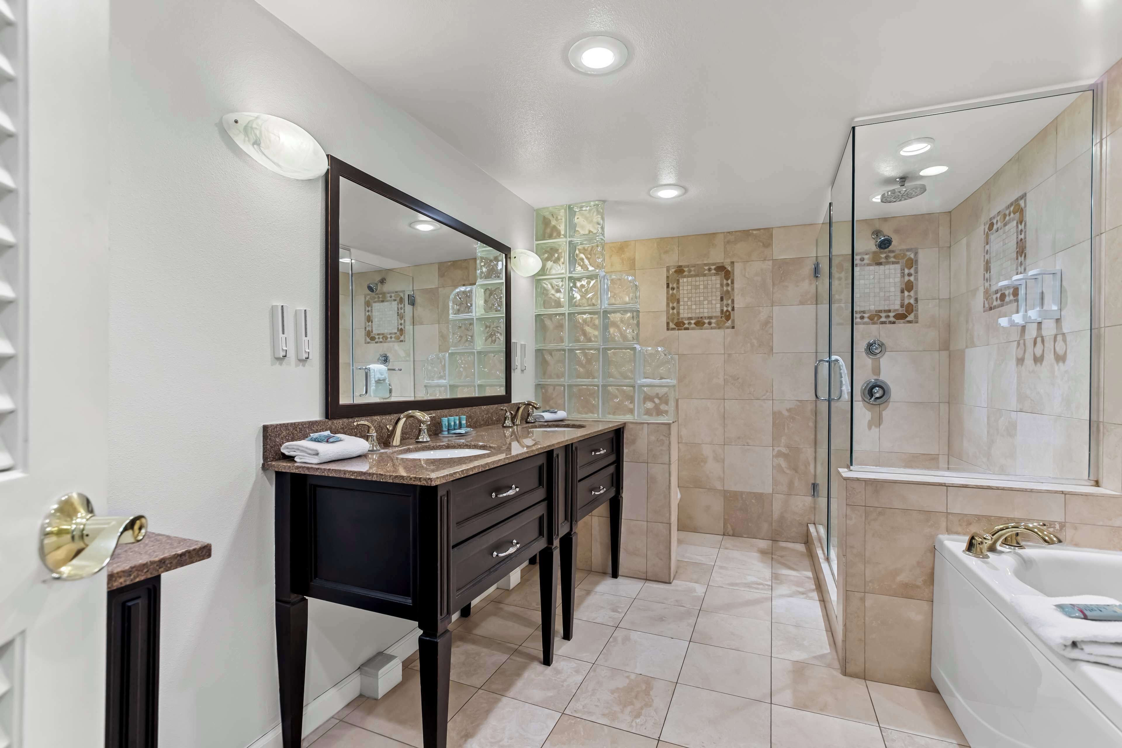 A modern bathroom with a double sink vanity, a glass shower enclosure, and a large bathtub.