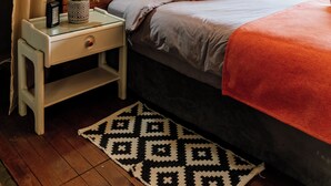 A cozy bedroom with a wooden headboard, a bedside table with a lamp, and a patterned rug. - Rocky Drift Private Nature Reserve (Emgwenya)