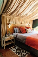 Um quarto acolhedor com cabeceira de madeira, mesa de cabeceira com abajur e tapete estampado.