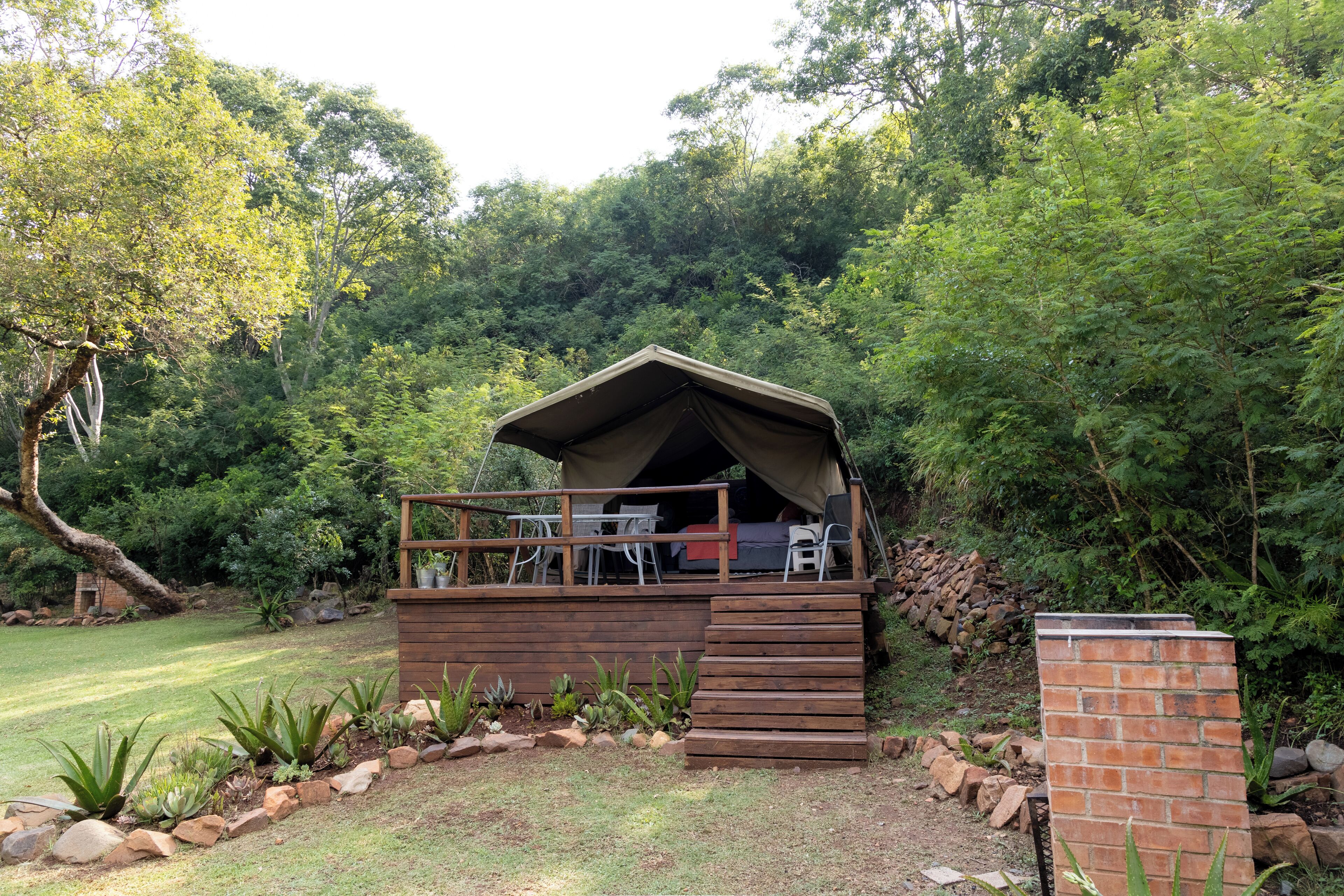 Una terraza de madera con una estructura cubierta, rodeada por un jardín con rocas y plantas.