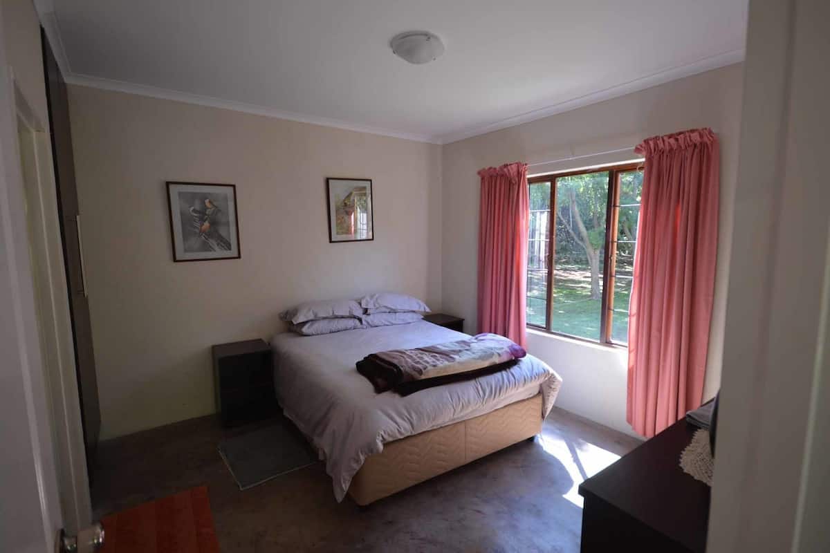 A bedroom with a bed, a window with curtains, and two framed pictures on the wall.