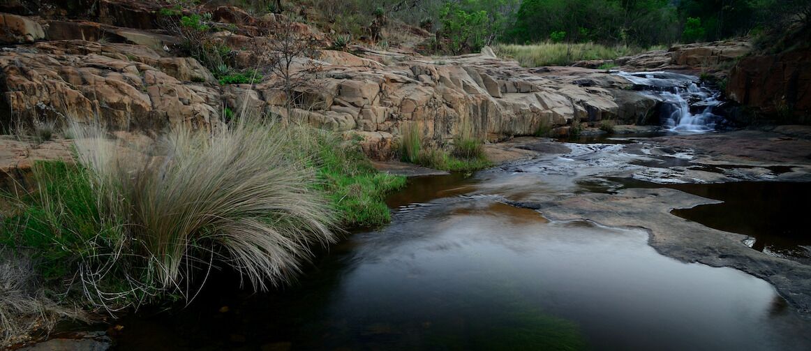 A natural landscape with a stream, rocky terrain, and sparse vegetation.