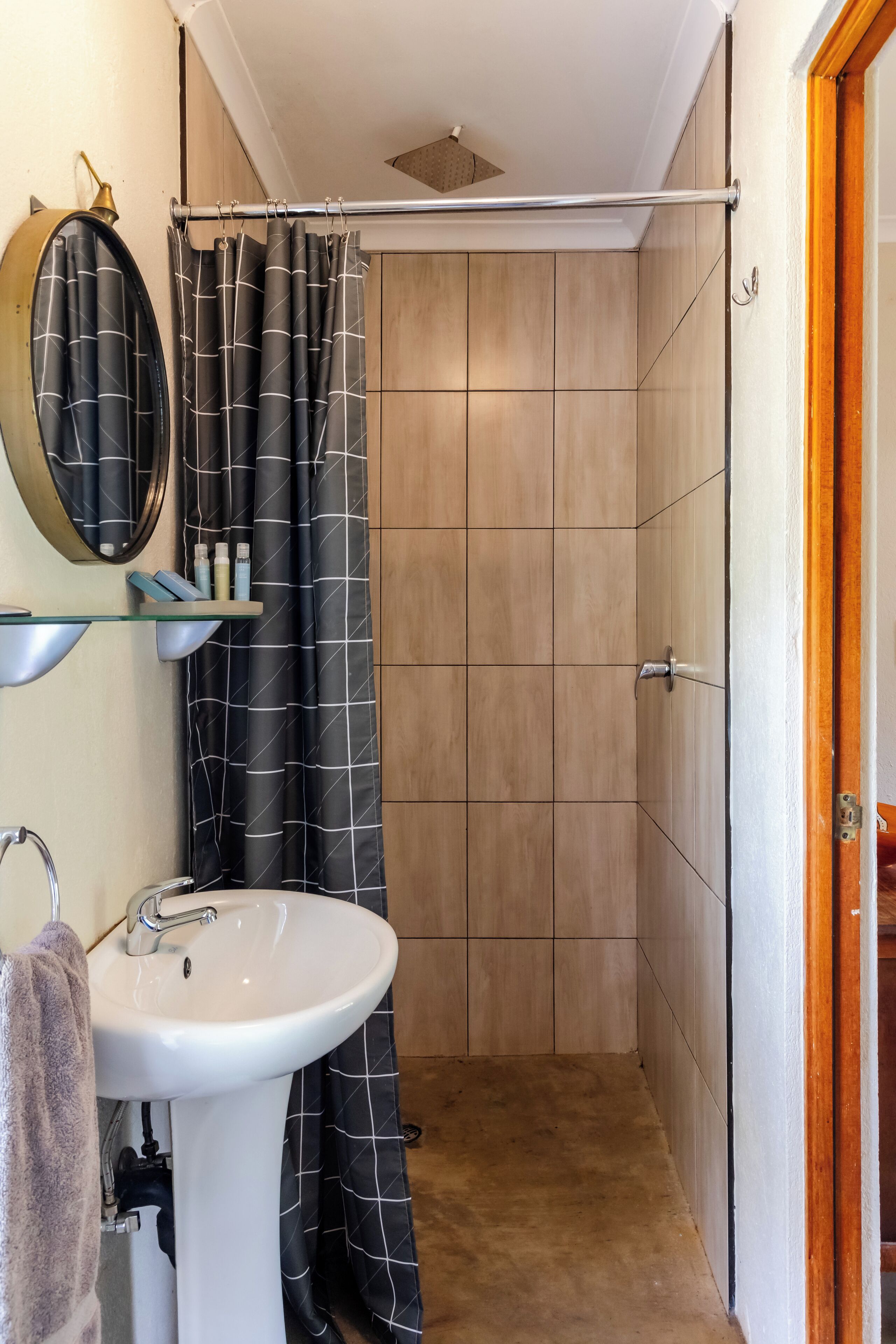 A bathroom with a white sink, a mirror, a shower curtain, and a glass shelf with toiletries.