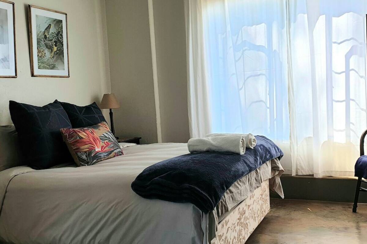 A bedroom with a bed, pillows, a lamp, and framed pictures on the wall.