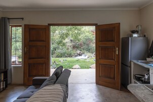 Una habitación con un sofá frente a una puerta de madera que da a un jardín con cascada.