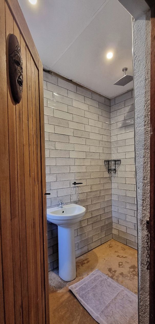 Un baño con lavamanos blanco, paredes con azulejos y zona de ducha.