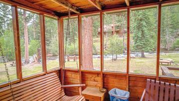 A wooden cabin with a porch, wooden benches, and a view of a forested area.