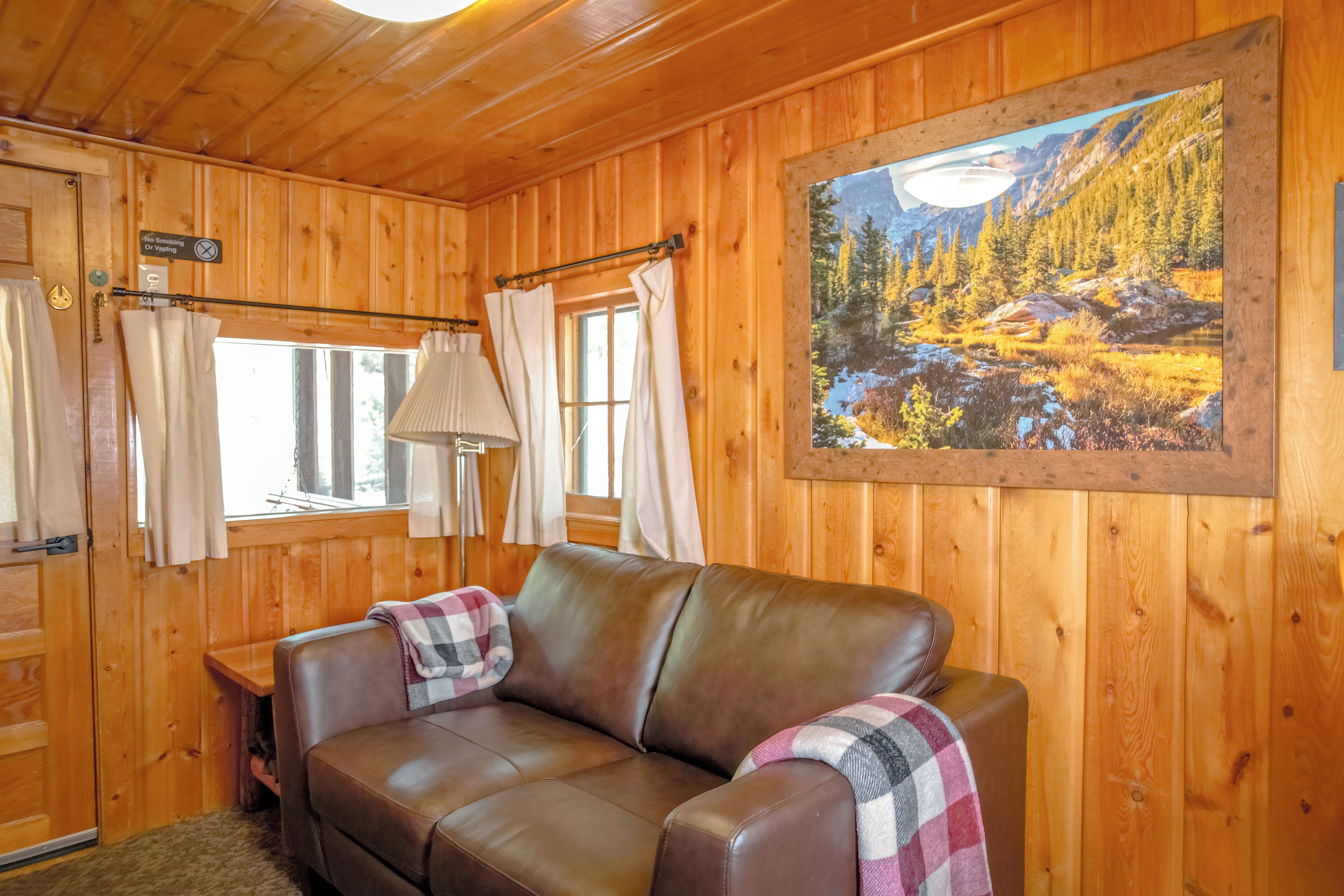 A cabin interior with a leather sofa, a painting of a forest landscape, and wooden walls.