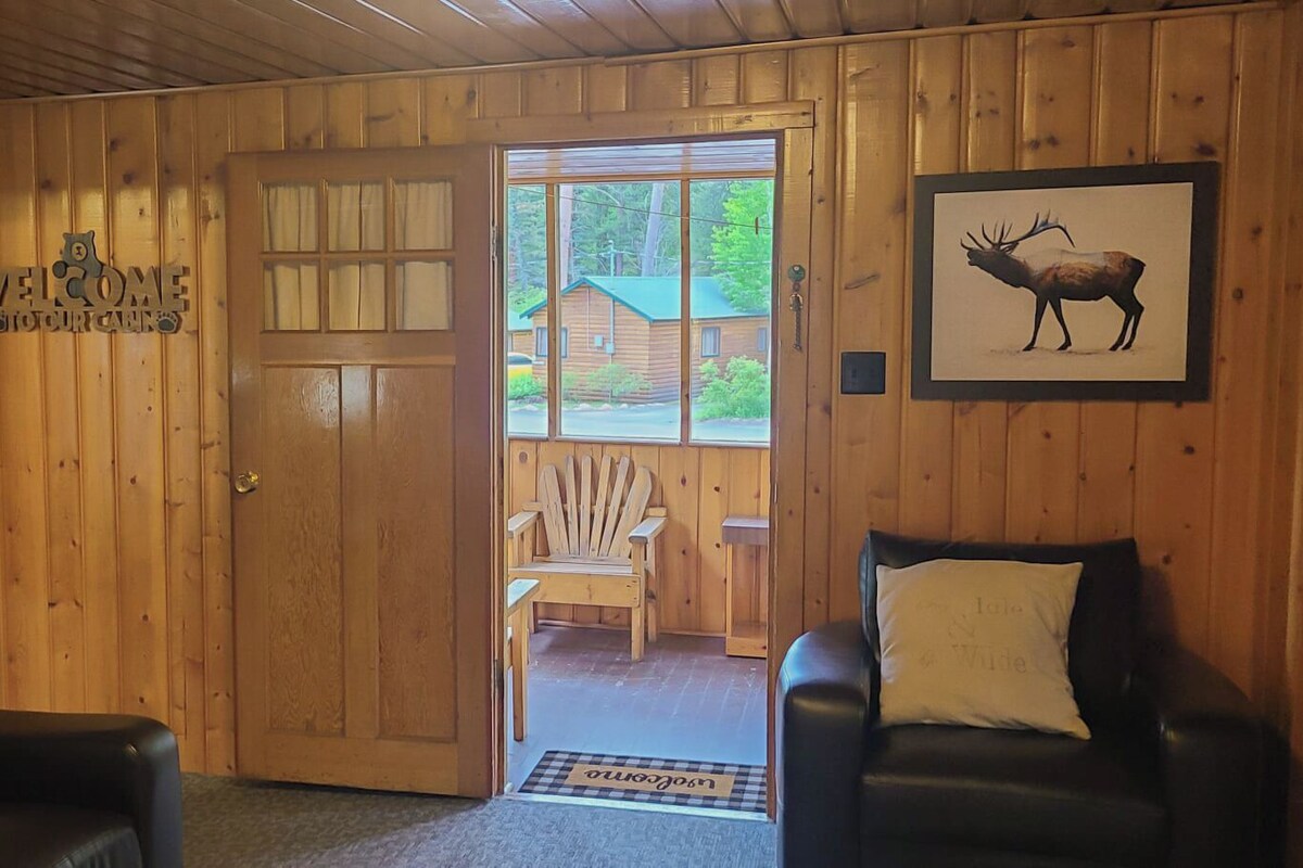 A wooden interior with two leather chairs, a door leading outside, and a framed moose picture.
