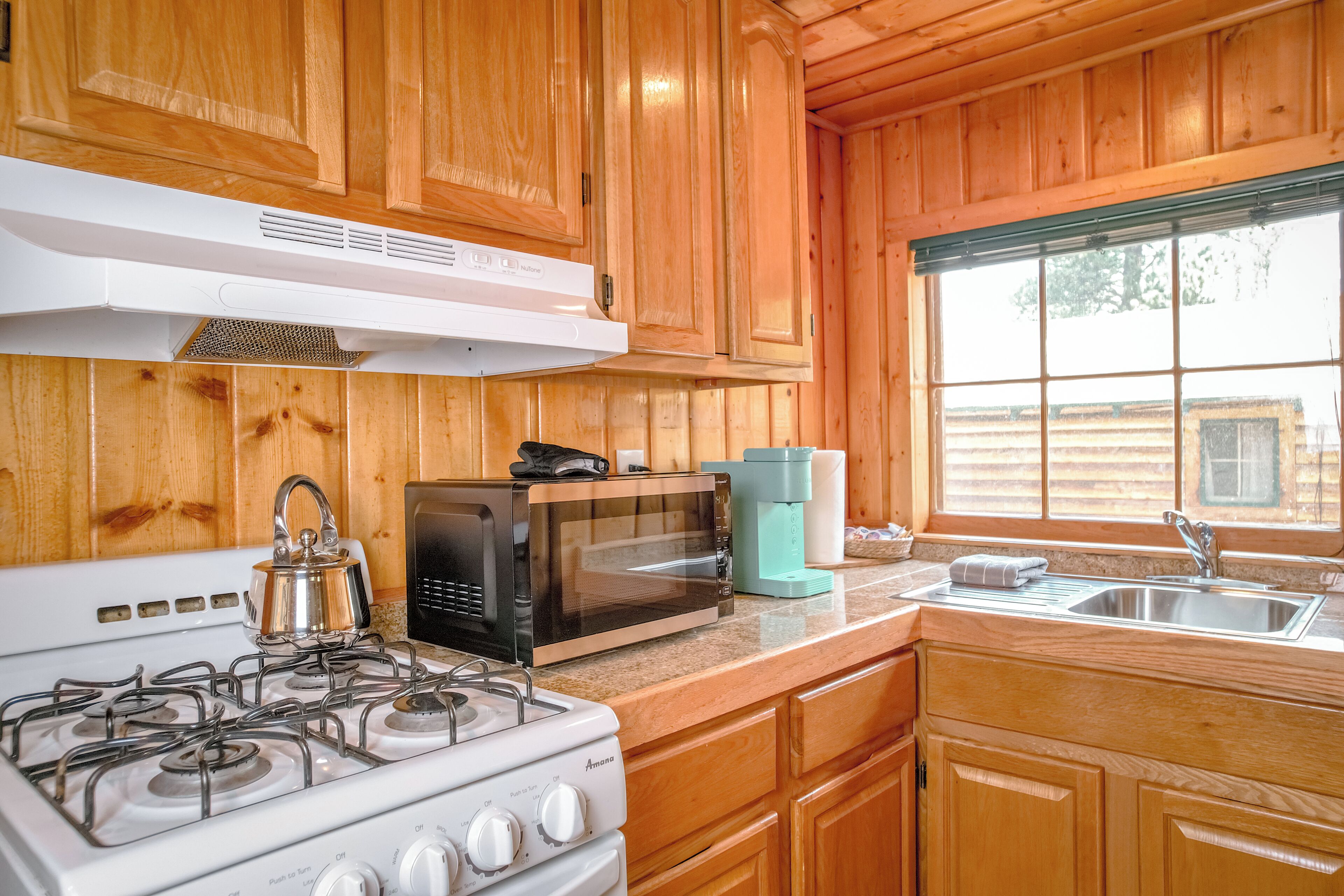 A kitchen with wooden cabinets, a stove, a microwave, and a coffee maker.