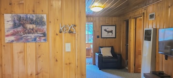 Un interno in legno con un quadro di un cervo, una segnaletica con la scritta 'KEYS', un divano in pelle nera e un televisore.