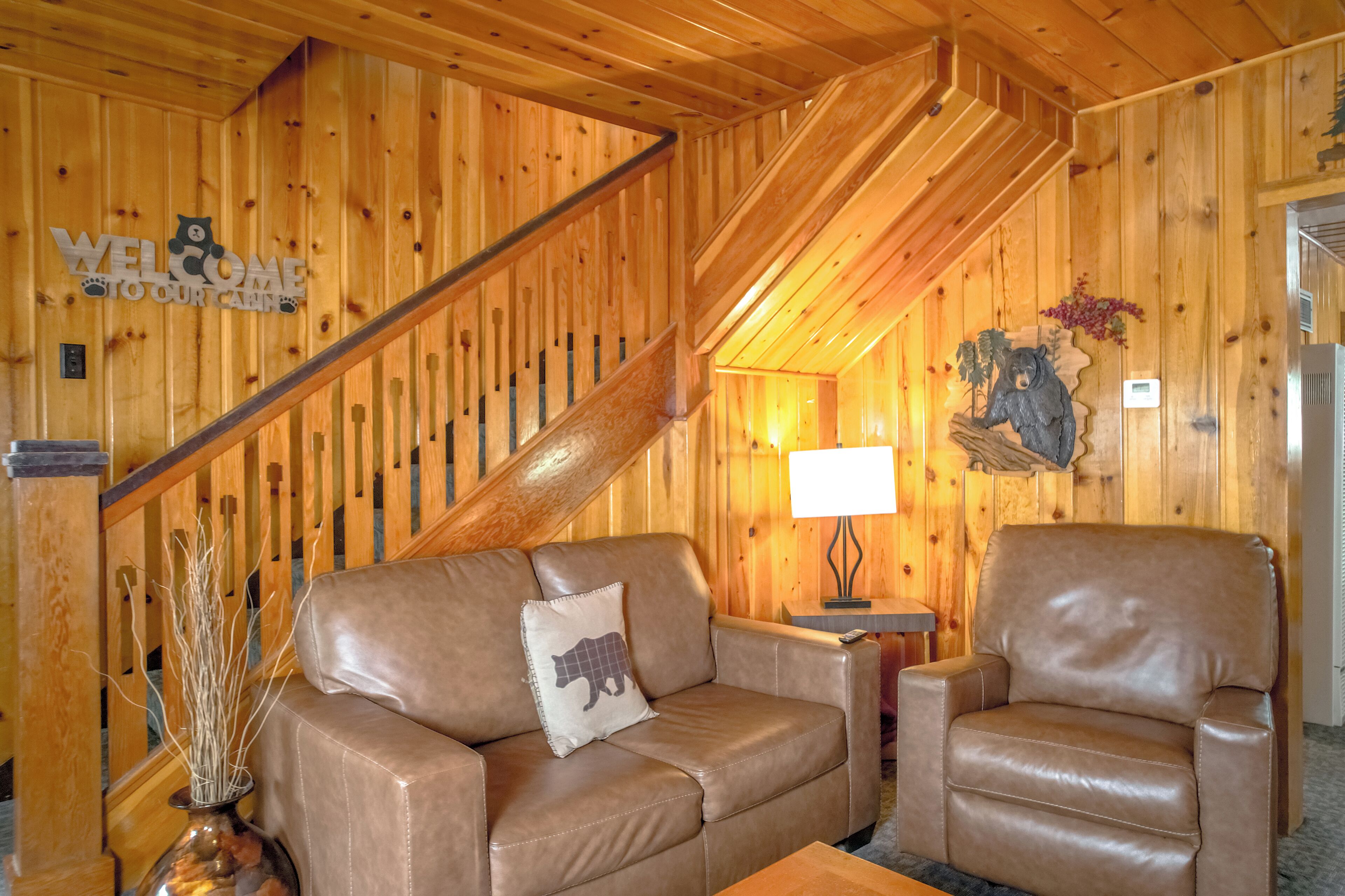 Un intérieur en bois avec un escalier, des meubles en cuir, une lampe et une décoration représentant un ours.
