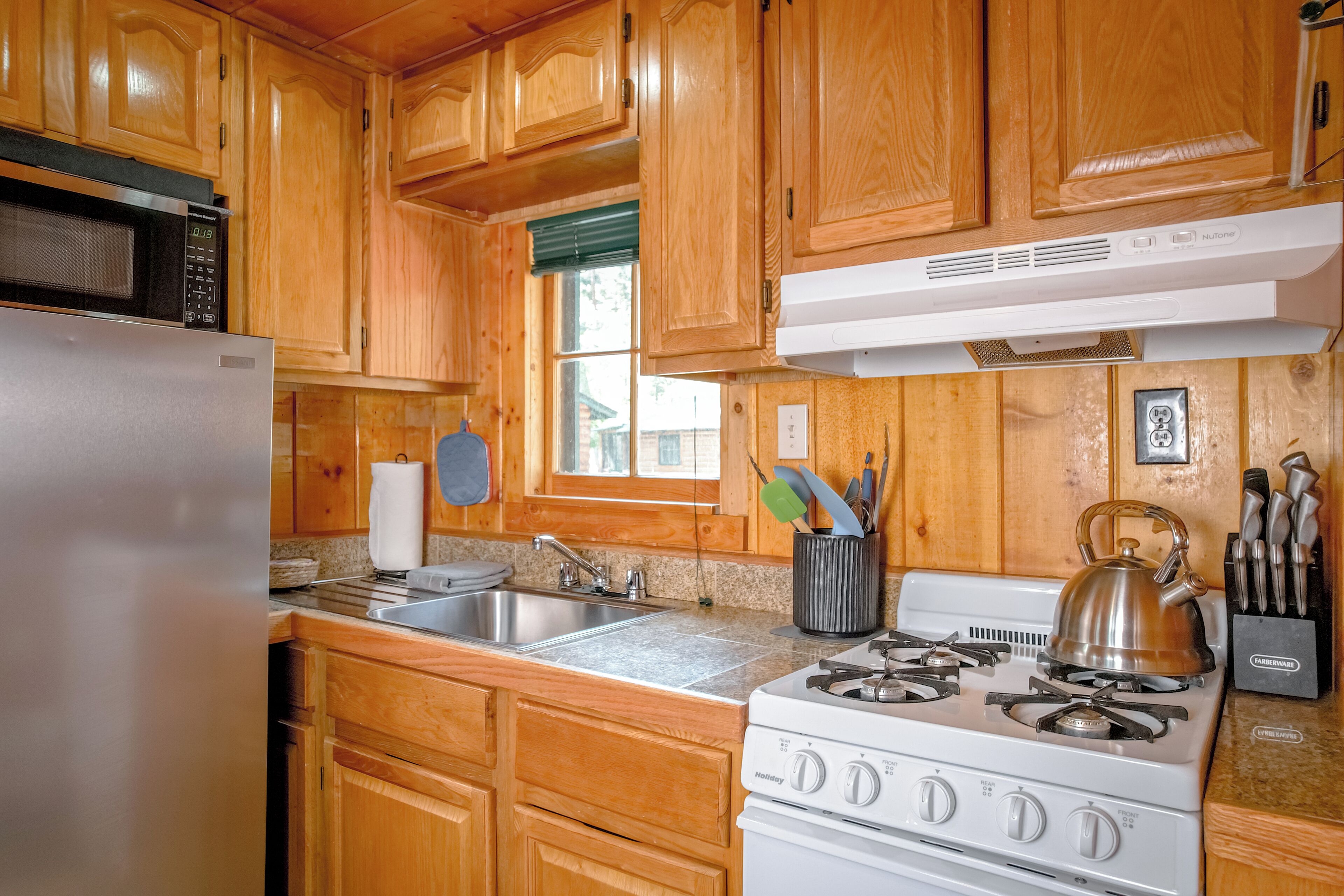 A kitchen with wooden cabinets, a stainless steel sink, a stove, and a microwave.