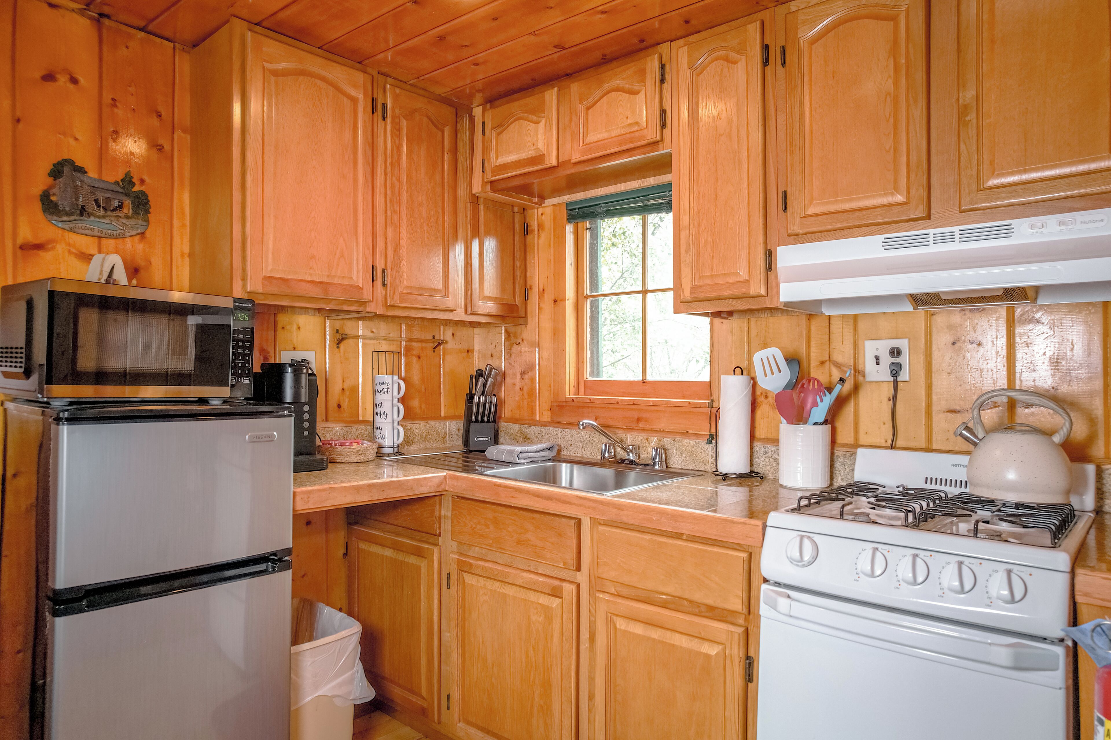 A kitchen with wooden cabinets, a microwave, a refrigerator, a stove, and a window.