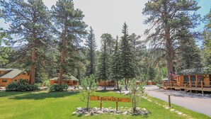 A lodge named Idlewilde with a sign in front, surrounded by tall pine trees and a clear sky. - Idlewilde by the River (Estes Park)