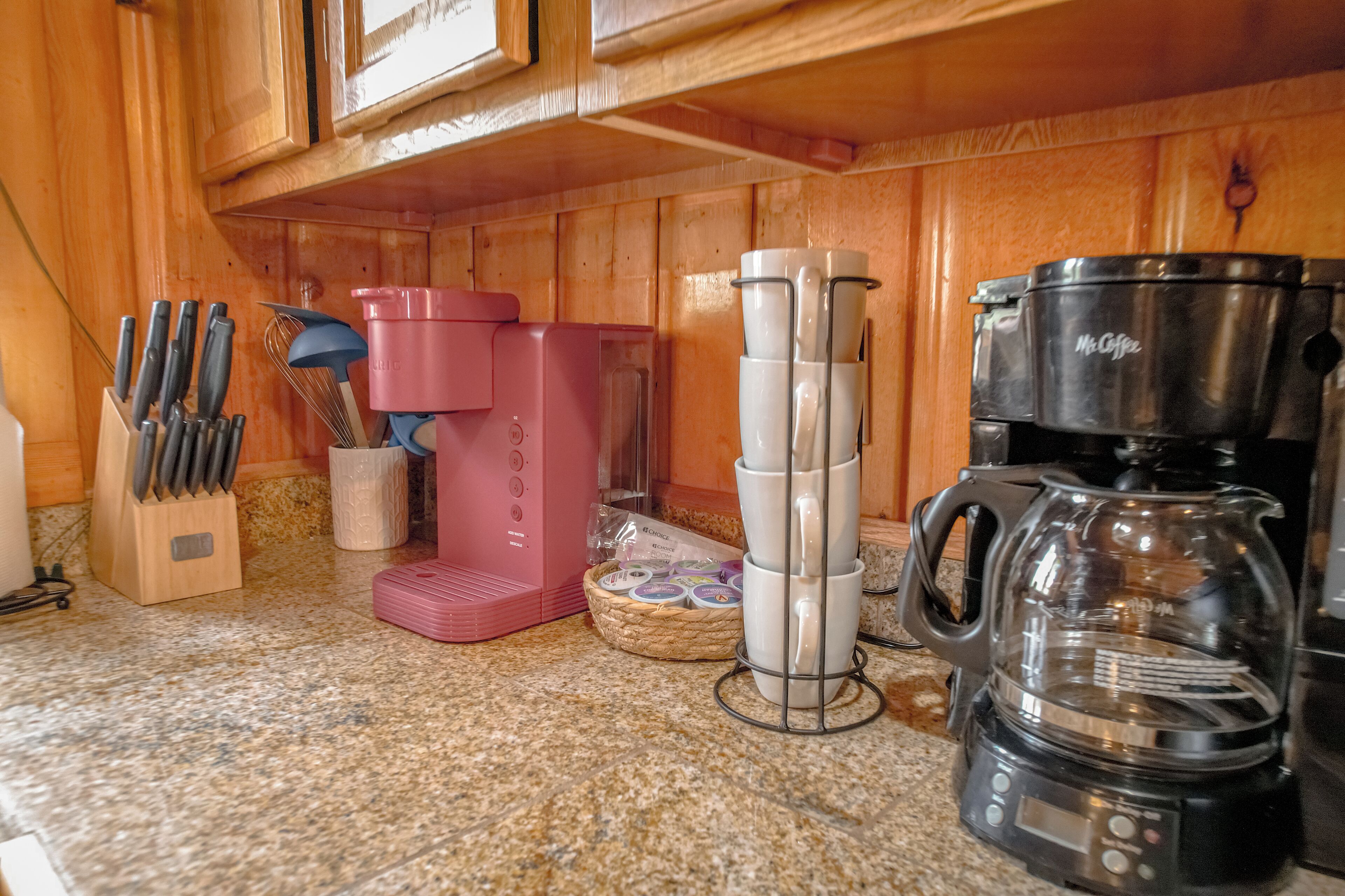 A kitchen with wooden cabinets, a coffee maker, a pink appliance, and a knife block.