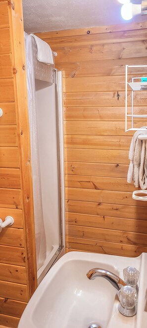 A wooden-paneled bathroom with a shower, a sink, and a towel rack. - Idlewilde by the River (Estes Park)