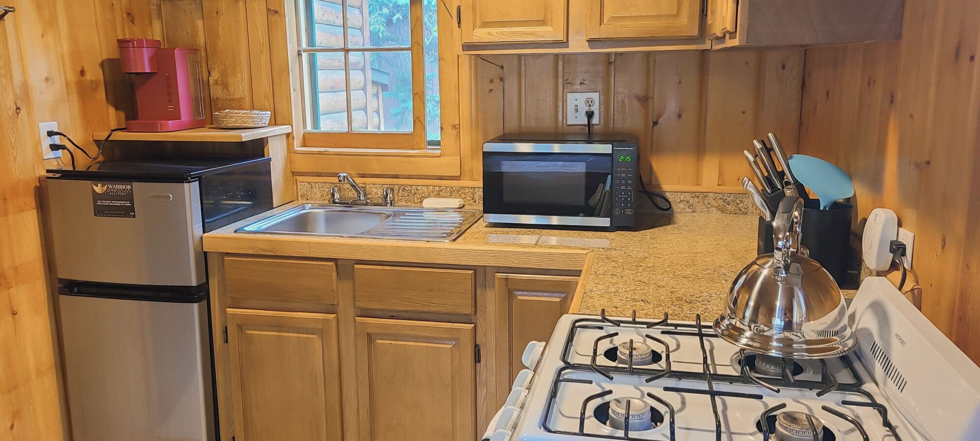 A compact kitchen with wooden cabinets, a refrigerator, a microwave, a stove, and a sink.