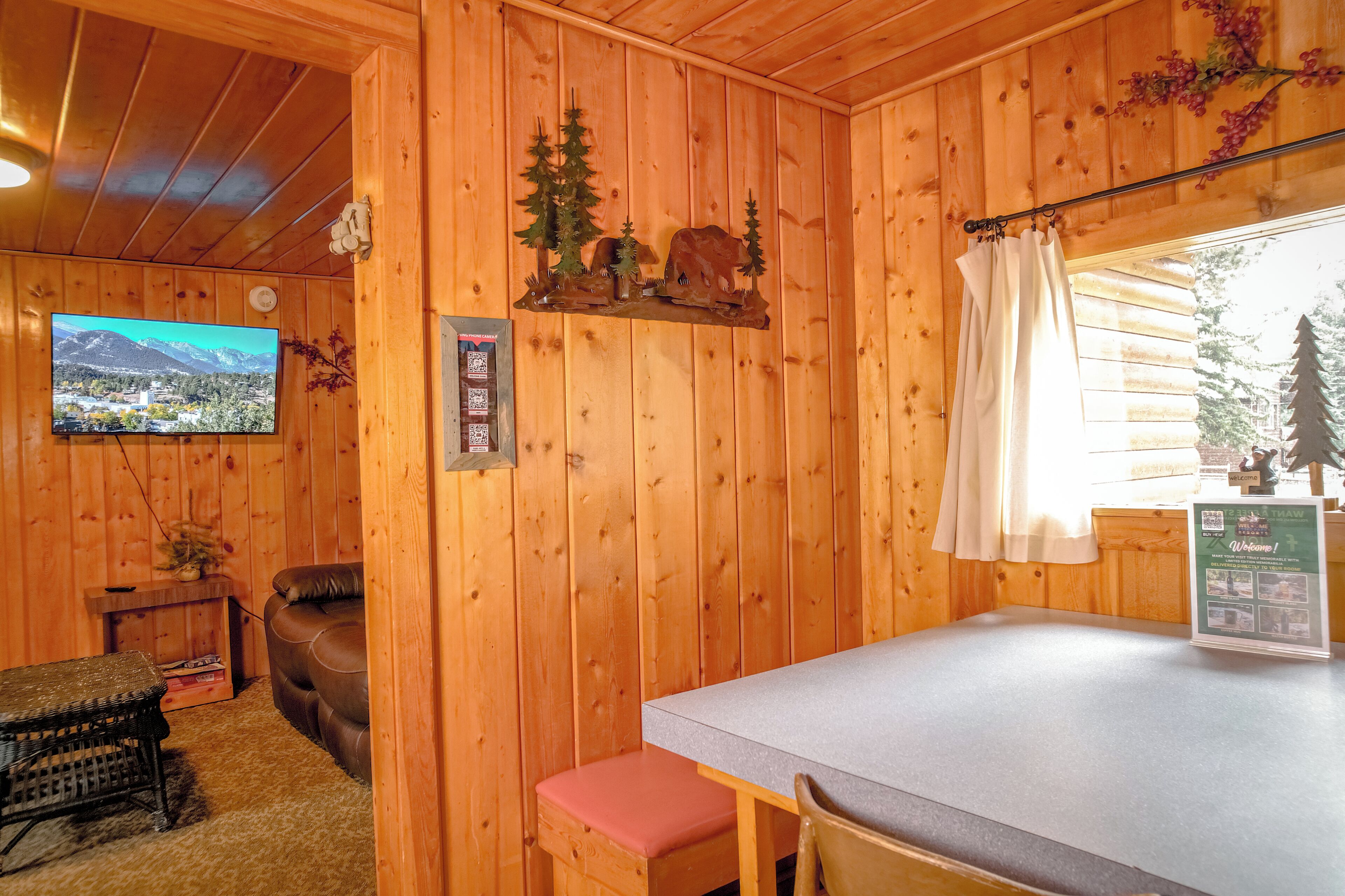 A wooden cabin interior with a television, a table, and a window with a curtain.