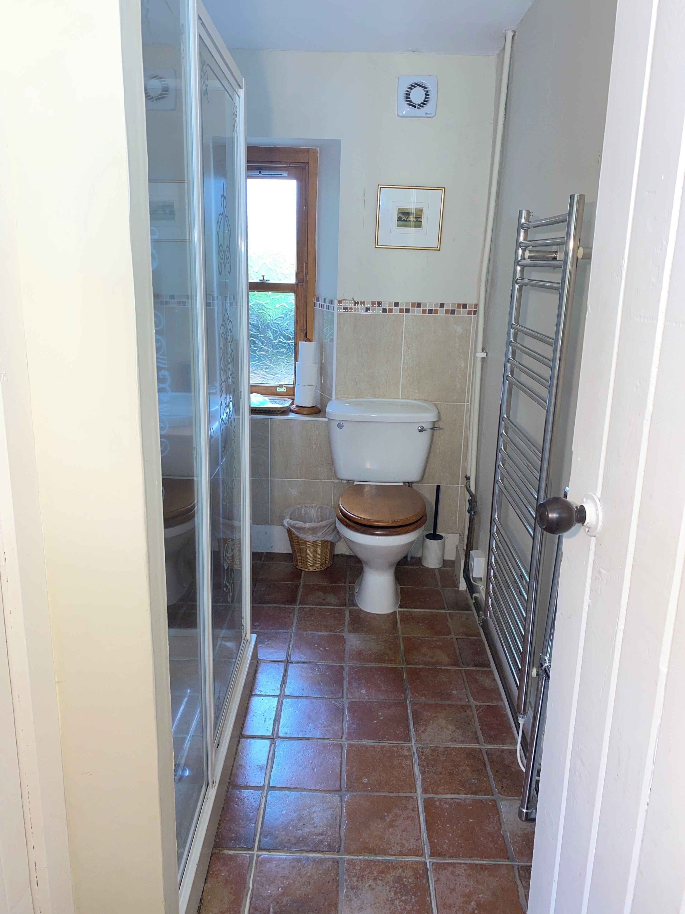 A bathroom with a toilet, a shower, a towel rack, and a window.