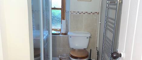 Une salle de bain équipée de toilettes, d’une douche, d’un porte-serviettes et d’une fenêtre.
