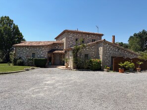 Une maison en pierre avec un toit en tuiles, une allée en gravier et des plantes en pot.