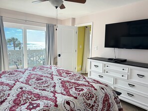 A bedroom with a bed, a dresser, a television, and a balcony with a view of the ocean.