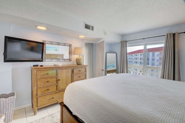A hotel room with a bed, a dresser, a television mounted on the wall, and a window with curtains.
