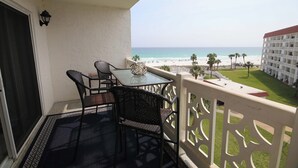 A balcony with a table and chairs, overlooking a beach with palm trees and a hotel in the background. - El Matador 358 -  FREE TICKETS!! Your stay includes free tickets to many area attractions! (Fort Walton Beach)