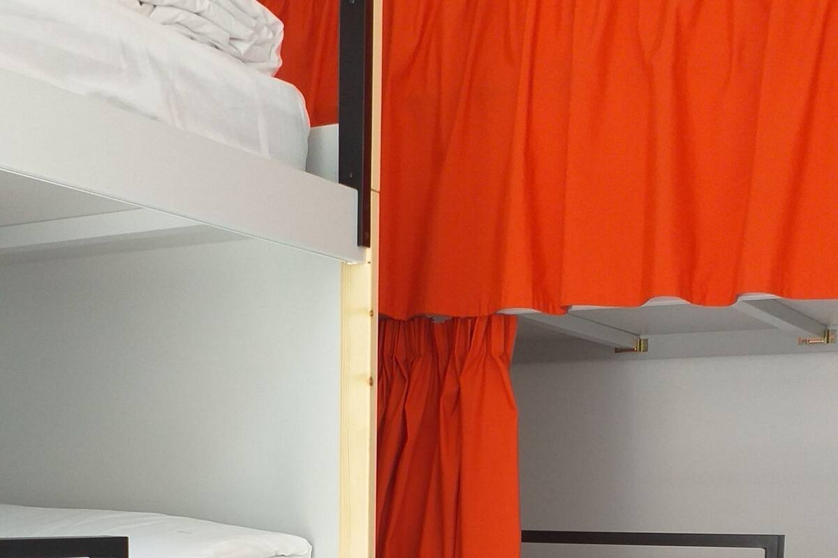 Dormitorio con literas, ropa de cama blanca y cortinas naranjas.