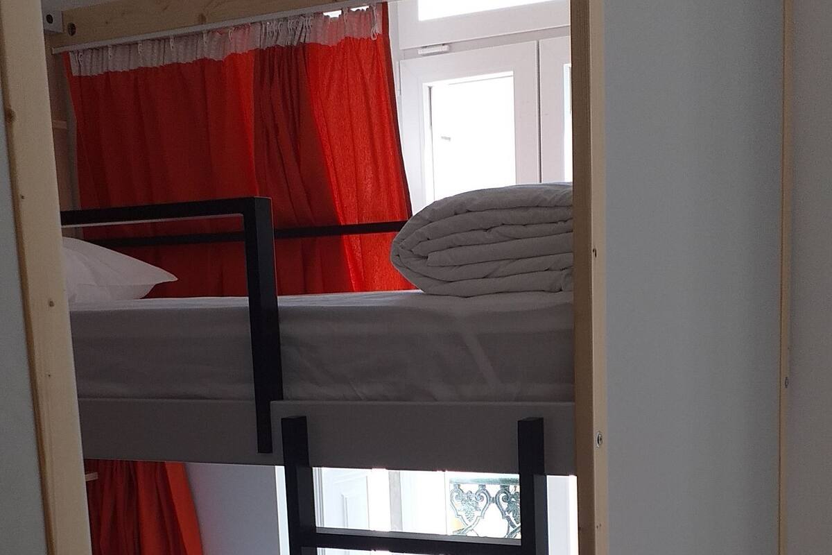 Una cama litera con estructura de madera y cortinas rojas.